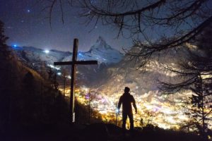 A person standing on top of a hill near a cross.