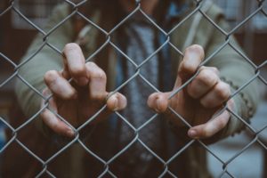A person is holding onto the chain link fence.