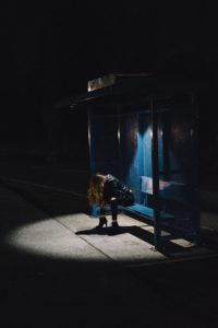 A person sitting on the side of a bus stop at night.