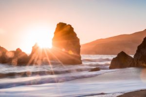 A sunset over the ocean with rocks in the foreground.