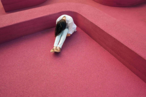 A woman sitting on the ground in front of a pink wall.
