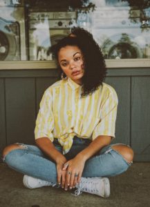 A woman sitting on the ground wearing jeans and a yellow shirt.