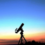 A telescope is silhouetted against the sky at sunset.