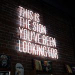 A brick wall with a neon sign that says " this is the sign you 've been looking for ".