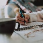 A person writing on paper with a pen.