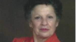 A woman in red shirt standing next to wall.