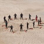 A group of people in wet suits standing on top of sand.