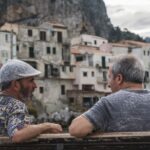 Two men sitting on a bench looking at each other.