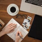 A person writing in a notebook on top of a wooden table.