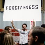 A man holding up a sign that says " forgiveness ".